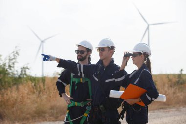 Ekip mühendisi rüzgar türbini işçi üniforması güvenlik anketi operasyon planlama yel değirmeni temiz enerjisini tartışıyor. Alternatif teknoloji çevreyi korur küresel ısınma sorunlarını azaltır.