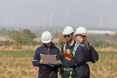 Dizüstü bilgisayarı tutan güvenlik üniforması giyen mühendis istasyon enerji rüzgârında yenilenebilir enerjiyle ilgili planı tartıştı. teknoloji çevreyi korur küresel ısınma sorunlarını azaltır.