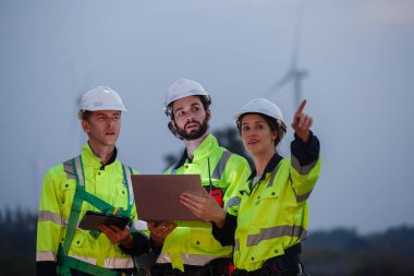 Team engineer wearing safety uniform holding laptop discussed plan about renewable energy at station energy power wind. technology protect environment reduce global warming problems.