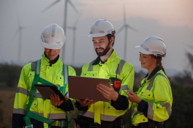 Team engineer wearing safety uniform holding laptop discussed plan about renewable energy at station energy power wind. technology protect environment reduce global warming problems.