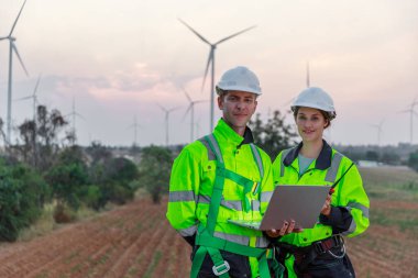 Dizüstü bilgisayarı tutan güvenlik üniforması giyen mühendis istasyon enerji rüzgârında yenilenebilir enerjiyle ilgili planı tartıştı. teknoloji çevreyi korur küresel ısınma sorunlarını azaltır.