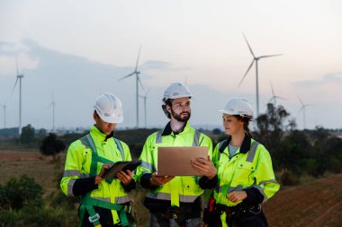 Dizüstü bilgisayarı tutan güvenlik üniforması giyen mühendis istasyon enerji rüzgârında yenilenebilir enerjiyle ilgili planı tartıştı. teknoloji çevreyi korur küresel ısınma sorunlarını azaltır.