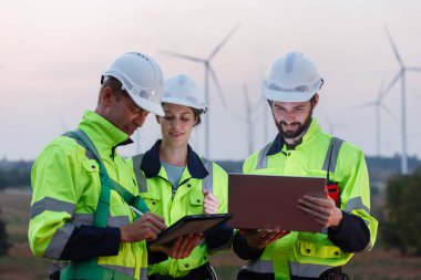 Dizüstü bilgisayarı tutan güvenlik üniforması giyen mühendis istasyon enerji rüzgârında yenilenebilir enerjiyle ilgili planı tartıştı. teknoloji çevreyi korur küresel ısınma sorunlarını azaltır.