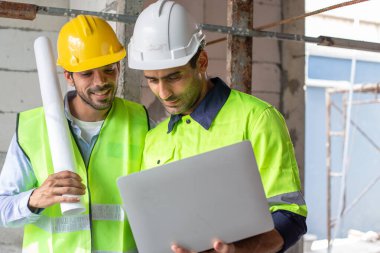 Profesyonel inşaat mühendisi ekibi, inşaat alanında duran kameraya bakan iki adam dizüstü bilgisayar giyiyor. Mimar ustabaşı işçi şefi.