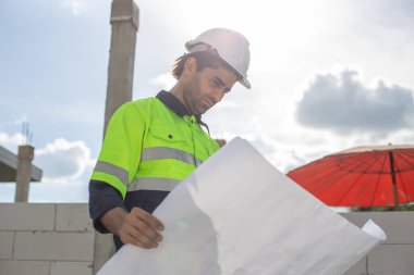 Adam mühendis, bina inşaatında şablon çizimi tutuyor. Erkek mimar ev inşaatında duruyor. Ustabaşı iş yerinde.