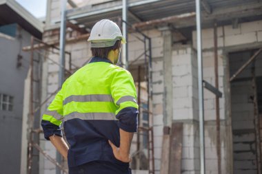 Mühendis evi inşaatının portresi miğfer ve güvenlik üniforması. Erkek mimar ev inşaatında duruyor. Ustabaşı iş yerinde.