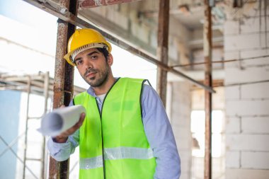 Ev inşaatçılarının portresi miğfer ve güvenlik üniforması üzerinde taslak çizimler var. Erkek mimar ev inşaatında duruyor. Ustabaşı iş yerinde.