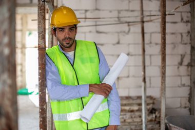 Ev inşaatçılarının portresi miğfer ve güvenlik üniforması üzerinde taslak çizimler var. Erkek mimar ev inşaatında duruyor. Ustabaşı iş yerinde.