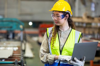 Kadın mühendis imalat fabrikasında çalışırken dizüstü bilgisayar kullanıyor. Kadın işçi teknisyen metal işçiliği otomatik mekanik enerji projesi.