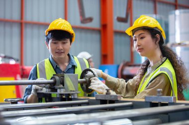 Erkek ve kadın mühendis fabrikada çalışırken şapka takıyor. Kadın teknisyen metal torna endüstrisini kontrol ediyor. Kadın atölye teknolojisi üretimi.