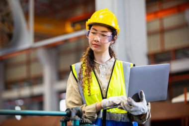 Kadın mühendis imalat fabrikasında çalışırken dizüstü bilgisayar kullanıyor. Kadın işçi teknisyen metal işçiliği otomatik mekanik enerji projesi.