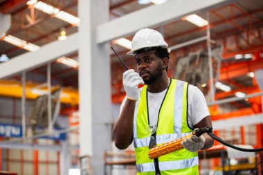 Üniformalı, güvenlik kilidi takan erkek Afrikalı Amerikalı işçi telsizi endüstriyel vinci kontrol etmek için kumandayı kullanıyor. Endüstriyel vinç teknisyeni..