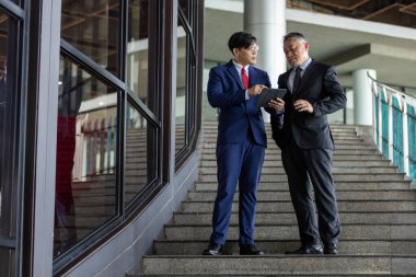 Asyalı çok nesilli iş adamları birlikte çalışırken takım elbise giyerler. Kıdemli ve genç işadamı ortaklar ve bağlantılarla toplantılara giderken anlaşmaları tartışıyor. İş stratejisini tartışın.