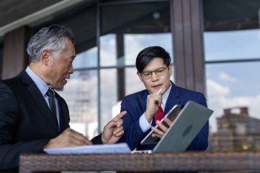 Asyalı çok nesilli iş adamları birlikte çalışırken takım elbise giyerler. Kıdemli ve genç iş adamları ortaklar ve bağlantılarla yapılan anlaşmaları tartışıyor. İş stratejisini tartışın.