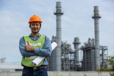 Asyalı işçi santral fabrikasının portresi. Taslak başparmak havada ve gülümsüyor. Güvenlik üniforması kaskı takan bir mühendis. Adam elektrik jeneratörü onarım operasyonları. elektrikçi enerji endüstrisi