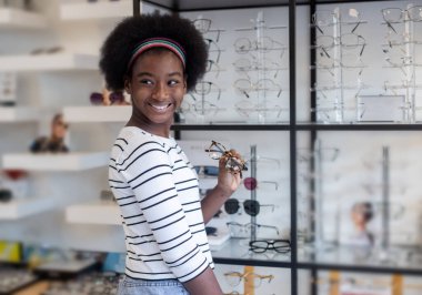 Portre mutlu genç kadın Afro-Amerikan saç tebessümü optik dükkanında duran gözlük takıyor. modern göz doktoru konsepti.