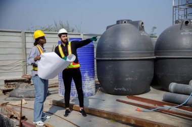 İnşaat mühendisi ve kadın Afro-Amerikan inşaat alanındaki iş kalitesini kontrol ediyor. Altyapı inşaatında çalışan çeşitli uluslardan oluşan bir ekip..