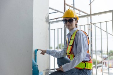 İnşaat mühendisi kadın tablet kullanarak içerideki su borularını ve inşaat alanının drenaj sistemini kontrol ediyor. Kadın işçi sarı başlıklı güvenlik boru hattı binanın içinde.