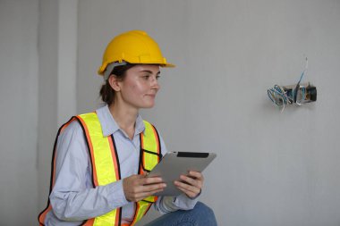 İnşaat mühendisi kadın tablet kullanıyormuş. Kalite kontrol, elektrik sistemi ofis binası. Kadın işçi sarı başlık emniyeti. İnşaat alanının altındaki odaya elektrik tesisatı kurun..