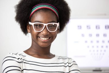 Mutlu genç Afrikalı Amerikalı gülümseyen kadın optik klinikte görme yeteneğini test etmek için optometrist kullanıyor..