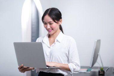 Genç bayan güzel Asyalı, pazarlama ofisinde dizüstü bilgisayar kullanarak çalışıyor. Mutlu iş kadını yönetici pozitif öğrenme projesinde çalışmaktan memnun.. 