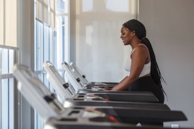 Spor salonunda koşu bandı koşan sağlıklı, güçlü, Afro-Amerikan kadın spor giyim egzersizi. Sporcu kadın motivasyonu spor koşusu kalorileri yakar.