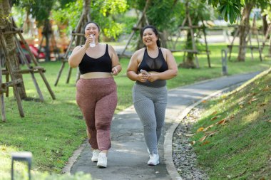 Neşeli iki fazla kilolu kadın spor giyimde bahçede egzersiz yaparken eğleniyor. Asyalı kızlar ve beden ölçüleri spor üniformaları giyiyorlar. Yeşil parkta egzersiz yapıyorlar. Sağlıklı bir kavram..