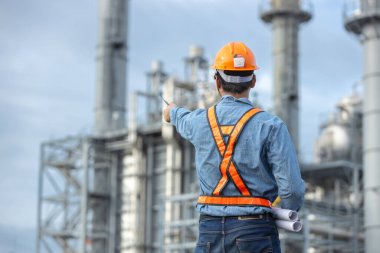 Asyalı işçi fabrikası planlarını tutuyor. İnşaat planının elektrik santralini işaret ediyor. Enerji petrokimya endüstrisinde güvenlik üniforması giyen mühendis..