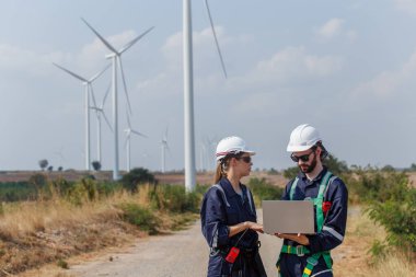 Team engineer wearing safety uniform holding laptop discussed plan about renewable energy at station energy power wind. technology protect environment reduce global warming problems.