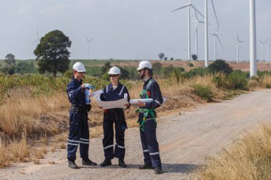 Ekip mühendisi rüzgar türbini işçi üniforması güvenlik anketi operasyon planlama yel değirmeni temiz enerjisini tartışıyor. Alternatif teknoloji çevreyi korur küresel ısınma sorunlarını azaltır.