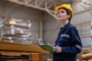 Kadın kağıt deposu çalışanı elinde bir pano tutarak depoda kaliteli karton bükülmüş kutuları kontrol ediyor. Kağıt üretiminde büyük endüstri.