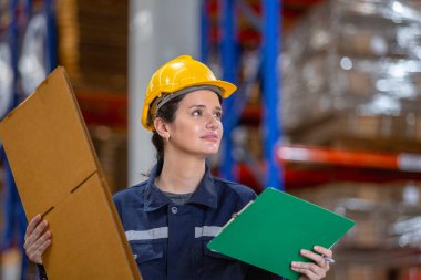 Kadın depo çalışanı elinde kağıt ürünleri ve pano kontrolü yapıyor. Kaliteli karton bükülmüş karton kutuları depoda kontrol ediyor. Kağıt üretiminde büyük endüstri.