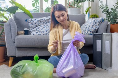 Evde oturan genç bir kadın kağıt ve plastik atıkları ayırıyor. Geri dönüşüm için çöp ayıklama. Küresel ısınmanın azaltılması. Çevre koruma kavramı.