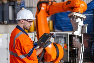 man engineer using remote robot controller operate standing at automation robot arms machine in factory. technician maintenance robotic workshop.