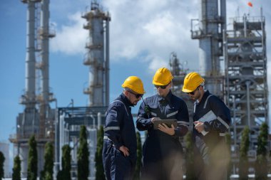 İstasyonda petrokimyayı rafine etmek için birlikte tablet kullanan bir mühendis. Teknisyen kalite petrol fabrikasını kontrol etti. Müfettiş rafineri binasının arka planında gaz bölgesinde duruyor..