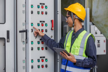 Elektrik mühendisi, santral ana Dağıtım Tahtaları kontrol paneli elektrik fabrikası binasını kontrol ediyor. Erkek Endüstriyel Teknisyen, güç dağıtım odasında çalışıyor..