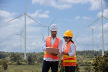 Team engineer wearing safety uniform holding laptop discussed plan about renewable energy at station energy power wind. technology protect environment reduce global warming problems.