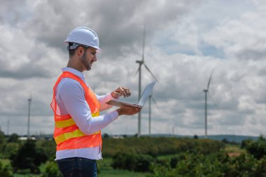 Dizüstü bilgisayarı tutan güvenlik üniforması giyen mühendis istasyon enerji rüzgârında yenilenebilir enerji ile ilgili planı tartıştı. teknoloji çevreyi korur küresel ısınma sorunlarını azaltır.