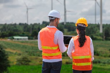 Team engineer wearing safety uniform holding laptop discussed plan about renewable energy at station energy power wind. technology protect environment reduce global warming problems.