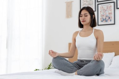 Güzel Asyalı kadınlar yoga yaparken asana nilüfer pozisyonu alırlar yatakta oturup dinlenirler ve evde sabahları esnerler. Rahatlama meditasyon sağlık konsepti