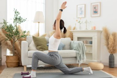 Genç Asyalı kadın omuz gerdirerek yoga yapıyor oturma odasında yerde oturuyor. Rahatla, rahatla ve evde egzersiz yap. Etkinlik vücut hareketi egzersizleri.