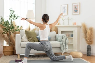 Genç Asyalı kadın omuz gerdirerek yoga yapıyor oturma odasında yerde oturuyor. Rahatla, rahatla ve evde egzersiz yap. Etkinlik vücut hareketi egzersizleri.