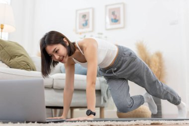 Genç Asyalı kadın omuz gerdirme, evde oturma odasında dizüstü bilgisayarla yoga çalışması. Rahatla, rahatla ve evde egzersiz yap. Etkinlik vücut hareketi egzersizleri.