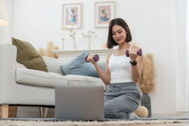 Asyalı genç kadın sabah egzersizleri evde dambıl tutarak el ele tutuşuyor, dinleniyor ve tatilde evde egzersiz yapıyor. Etkinlik vücut hareketi kolu.