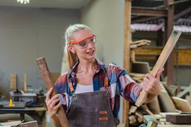 Genç marangoz kadın üniforma giyer ve gözlükler iş için uygun büyüklükte ve kaliteli ahşap seçer. Profesyonel zanaatkar konsepti. marangozluk endüstrisi.