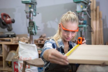 Genç marangoz kadınlar fiyonkçulukta mobilya yaparken, tahta görünümlü mezura kullanırlar. Ahşap fabrikasında zanaatkarlık mesleği. profesyonel mobilya ahşabı.