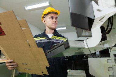 Adam kağıt deposu çalışanı bilgisayar sistemiyle birlikte depolama stoğundaki karton kutuları ve kaliteyi kontrol ediyor. Kağıt üretim hattındaki büyük endüstri.
