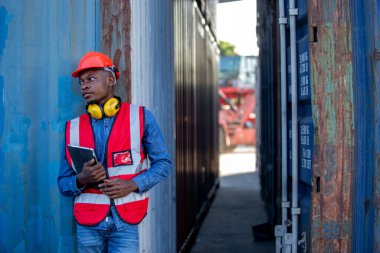 Male African American person foreman holding tablet standing containers loading. Industrial logistics import export and shipping.