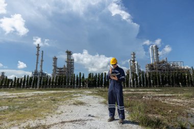 Profesyonel mühendis güvenlik üniforması ve rafine petrol petrokimya endüstrisinin yakınında bulunan tablet ve telsiz çalışma alanı tutan beyaz başlık giyer. Fabrika sitesi enerji santrali.