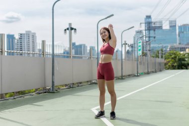 Genç ve güzel bir kadın spor kıyafetleri sabah koşusundan önce şehir parkında egzersiz yapıyor. Asyalı güçlü bayan spor kıyafetleri dışarıda esniyor. fitness sağlıklı konsept.